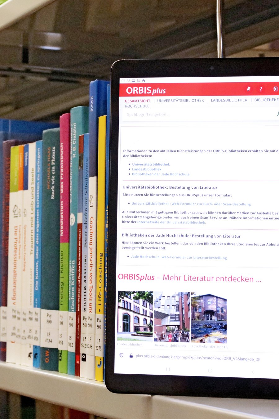 In einem Bücherregal steht ein Tablet, das den Online-Katalog ORBISplus zeigt.