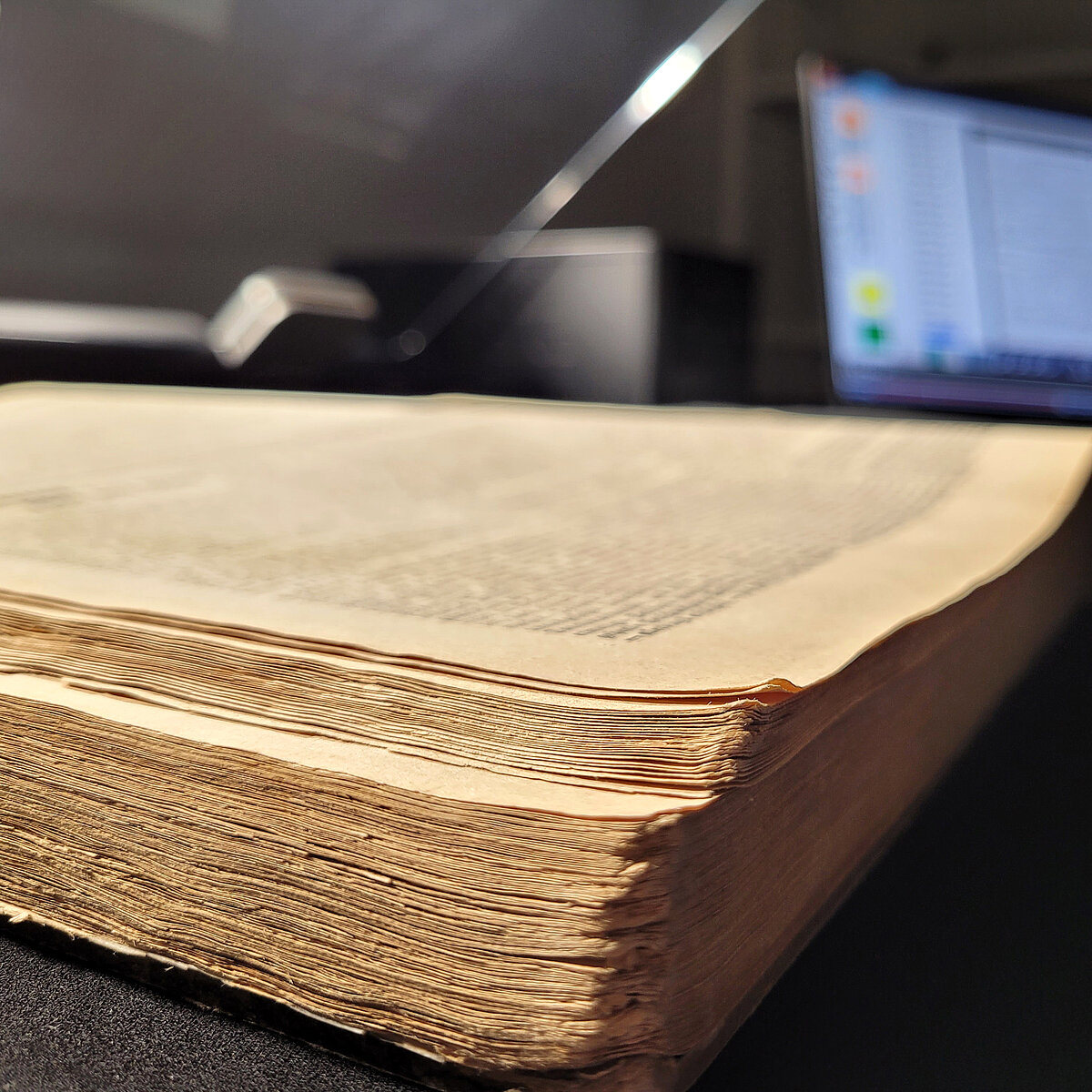 Detailaufnahme eines Zeitungsbandes in einem Buchscanner. Im Hintergrund unscharf ein Computerbildschirm.