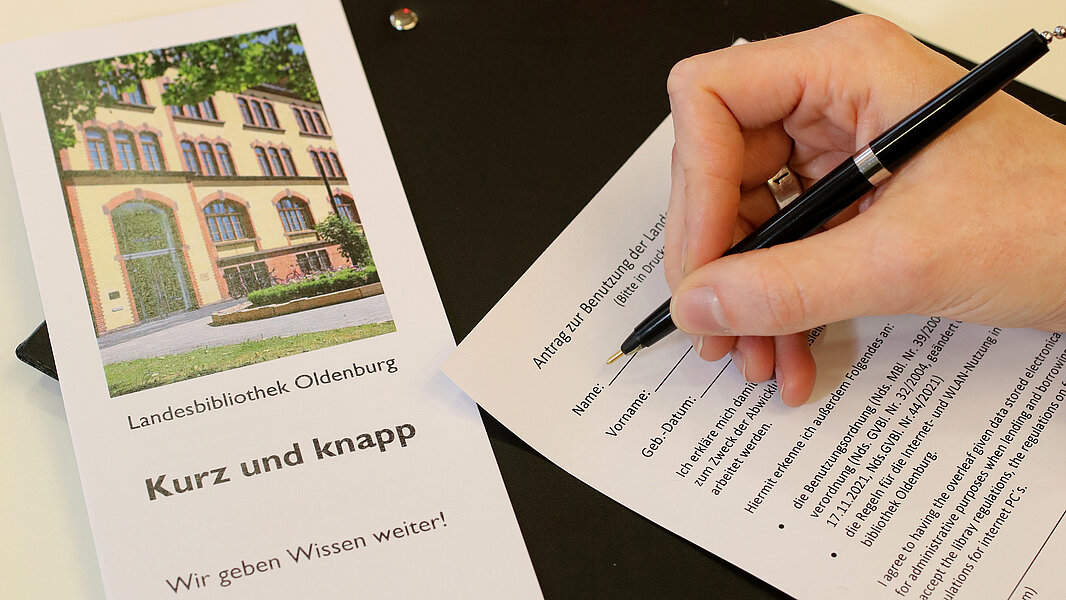 Eine Hand füllt das Anmeldeformular aus. Daneben eine Informationsbroschüre mit dem Titel "Kurz und knapp"