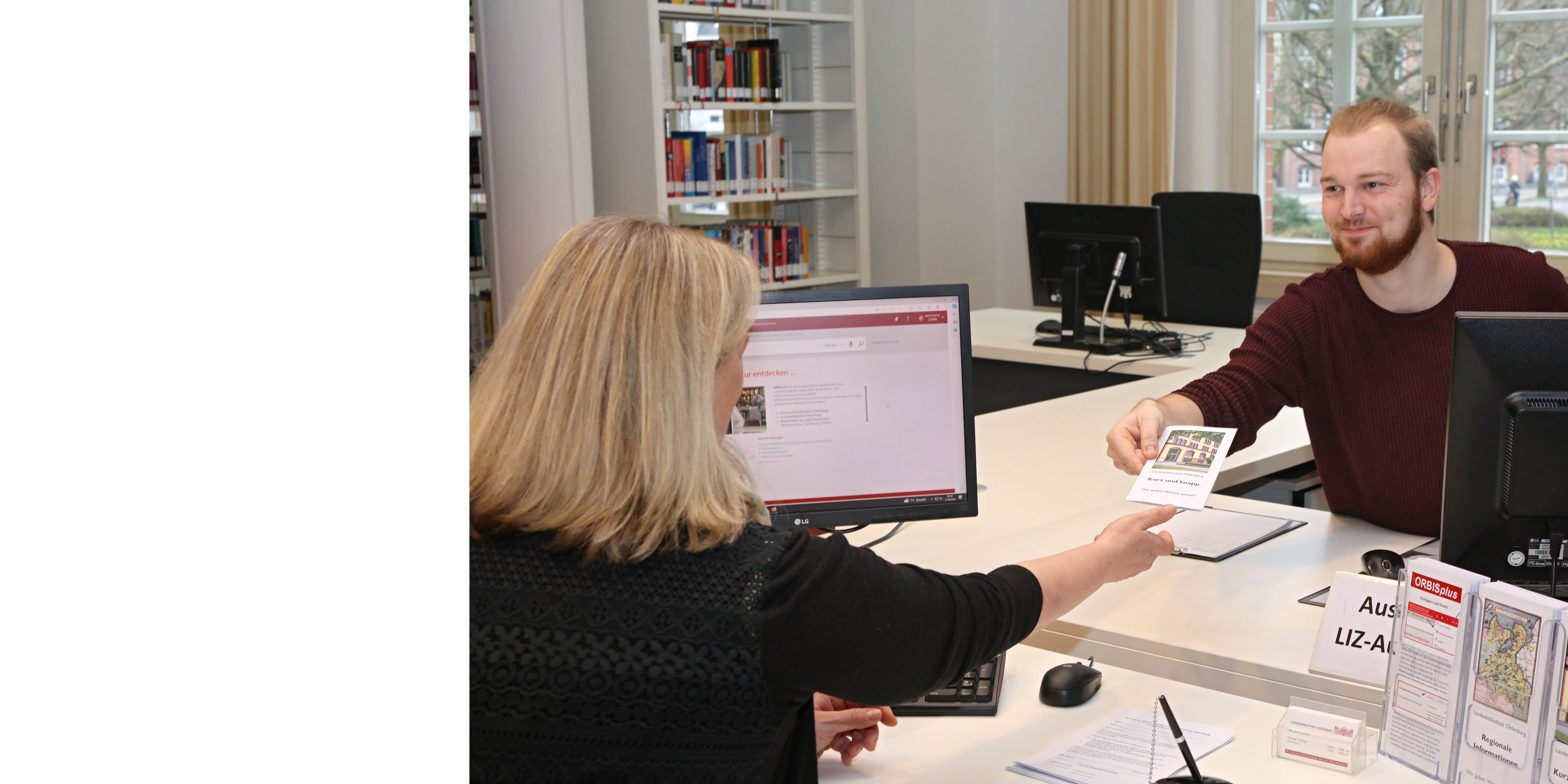 Ein Auskunftsmitarbeiter zeigt einer Nutzerin eine Infromationsbroschüre.