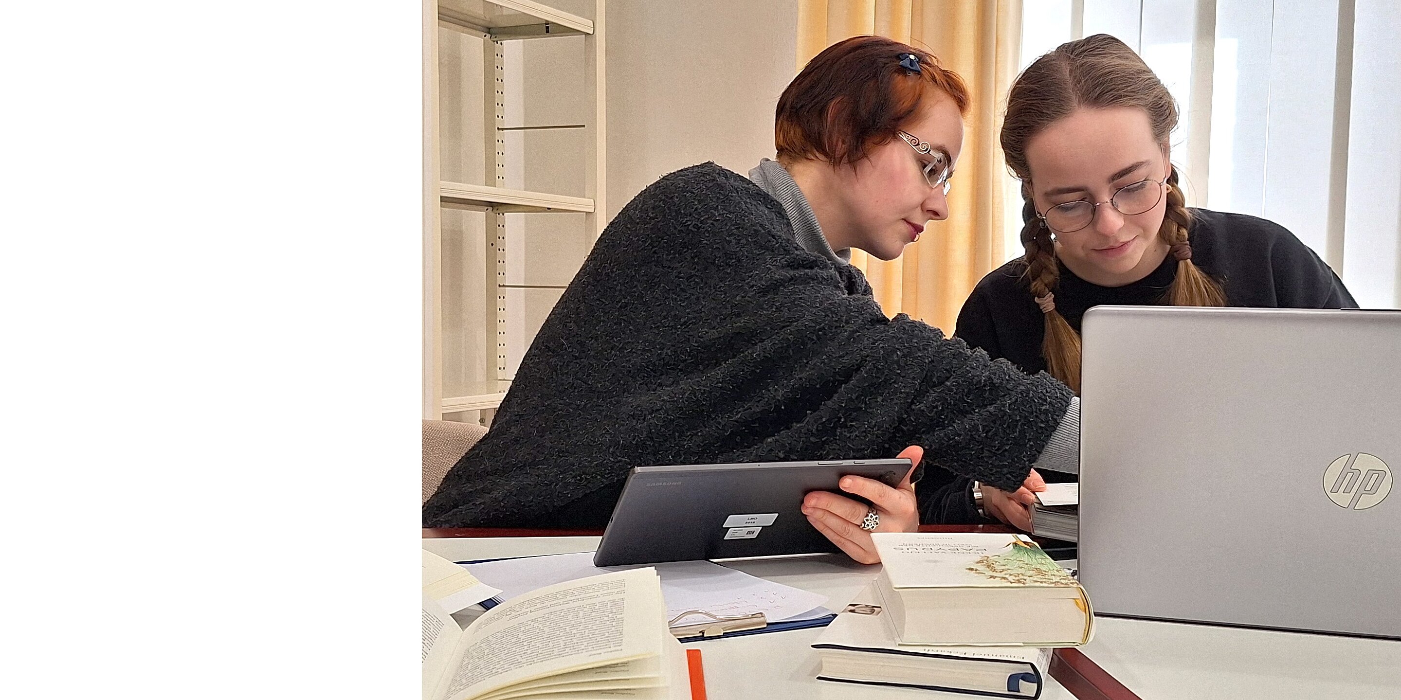 Zwei junge Frauen sitzen vor Laptop und Tablet.