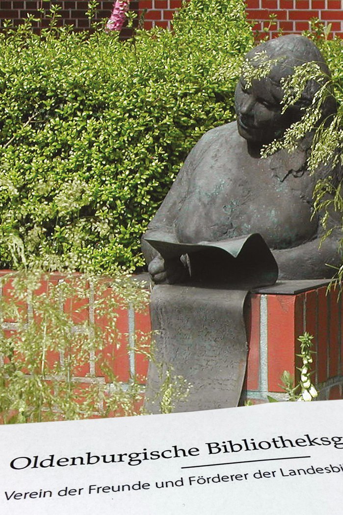 Blick auf eine Skulptur am Hintereingang der Landesbibliothek: Eine lesende Frau. Im Vordergrund ein Auszug aus einer Einladung der Oldenburgischen Bibliotheksgesellschaft.
