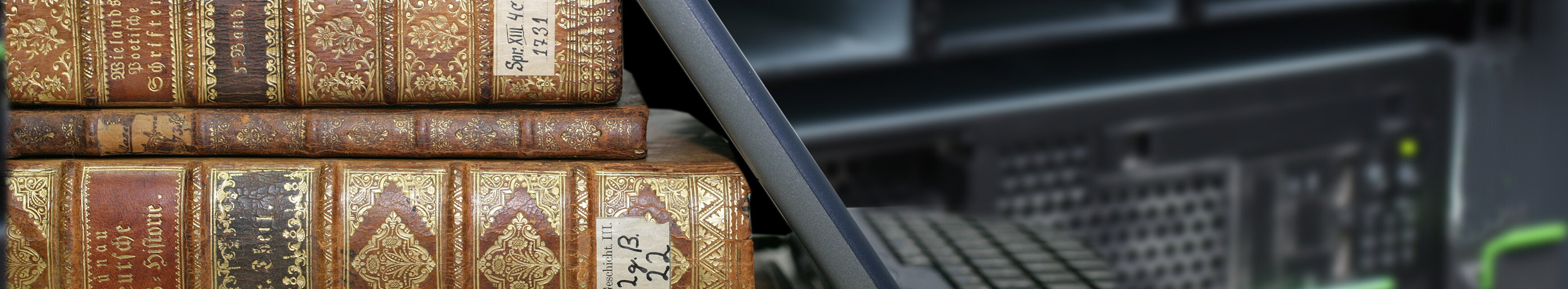 Ein Stapel historischer Bücher, an dem ein Laptop lehnt.