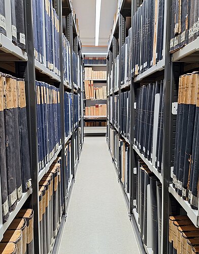 Blick durch Regalreihen mit Zeitungsbänden.