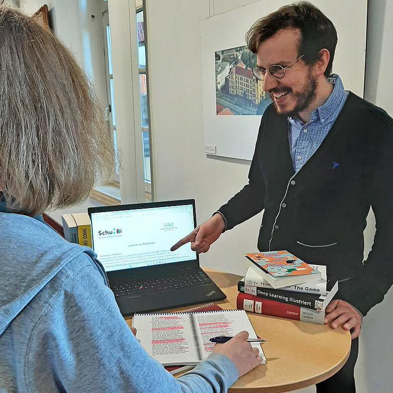Bibliotheksmitarbeiter berät Schüler am Laptop.