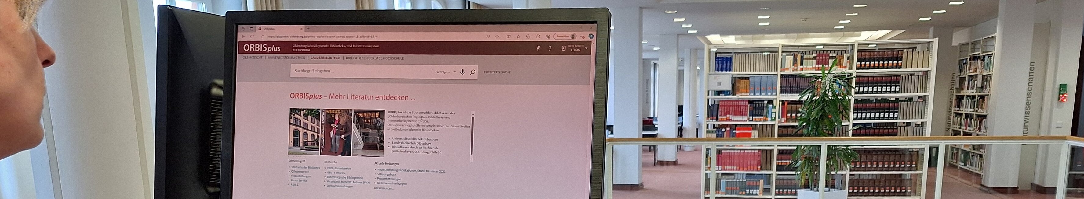 Im Vordergrund ein Bildschirm mit dem Online-Katalog ORBISplus. Im Hintergrund Regalreihen.
