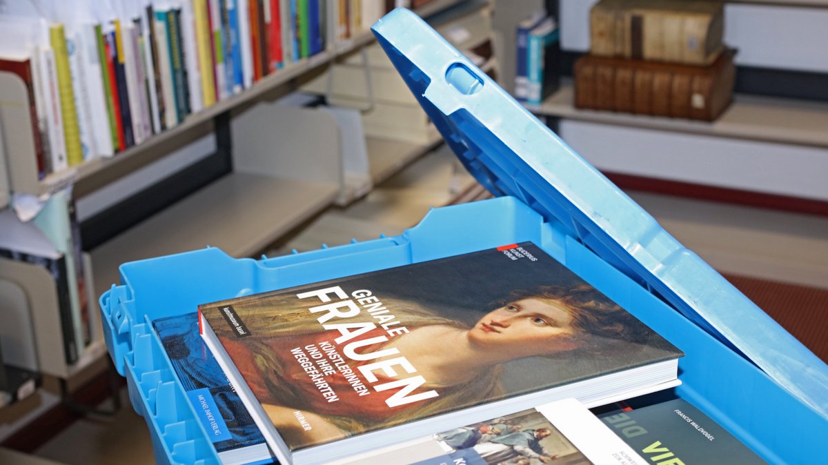 Blick in eine blaue Bücherkiste. Darin Bücher. Im Hintergrund Bücher in Regalen.