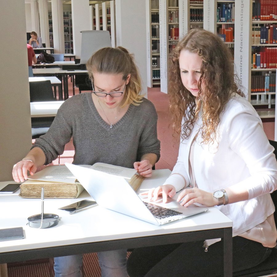 Zwei Schülerinnen sitzen am Tisch im Lern- und Informationszentrum und lernen.