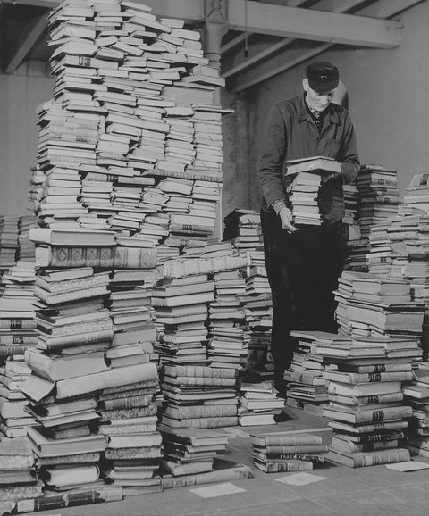 Historisches Foto: Ein Mann steht zwischen aufgetürmten Büchern (Ofener Straße 1946)