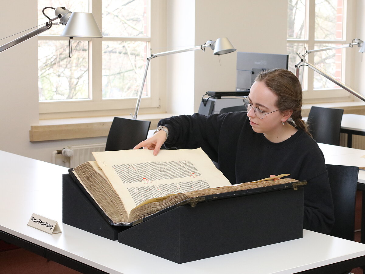 Nutzerin am Rara-Arbeitsplatz. Ein großformatiges Buch liegt auf zwei Schaumstoffkeilen.