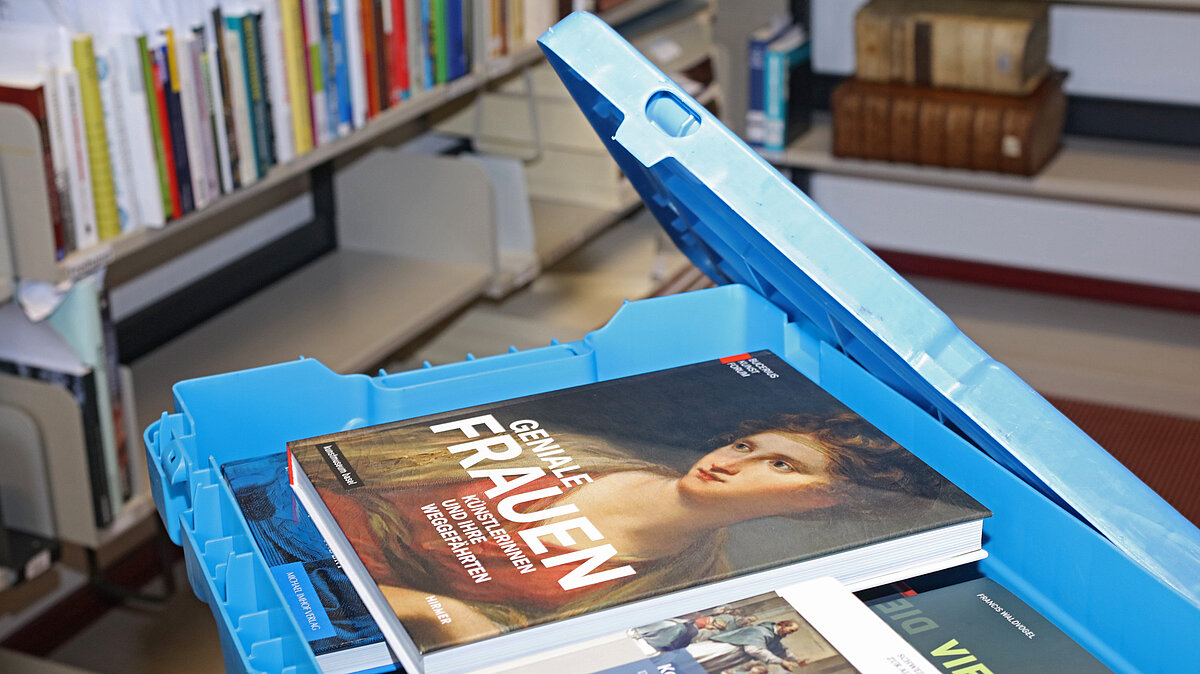 Blick in eine blaue Bücherkiste. Darin Bücher. Im Hintergrund Bücher in Regalen.