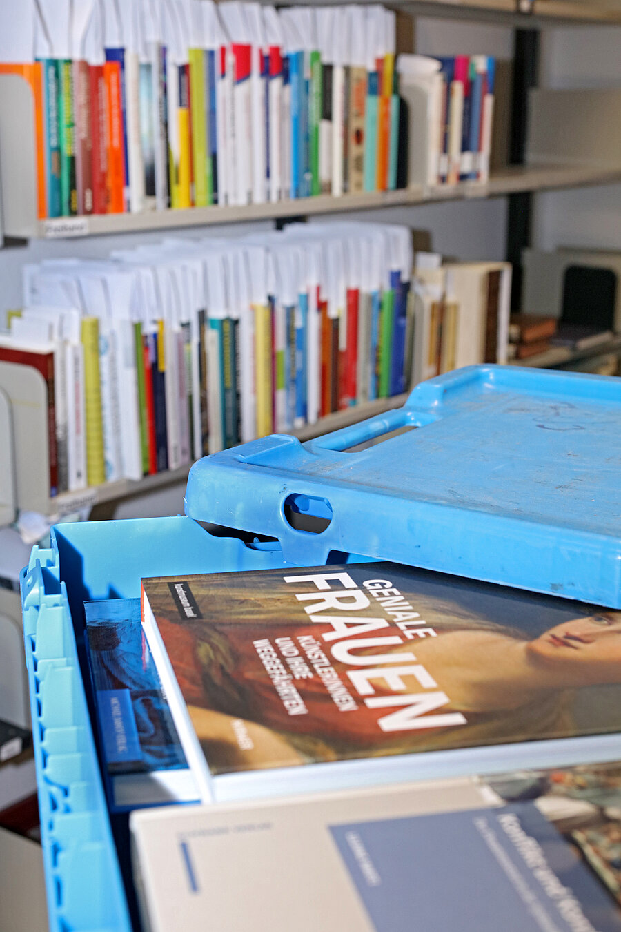 Blick in die offene, blaue Bücherkiste. Darin Bücher aus der Fernleihe. Im Hintergrund Bücher im Regal.