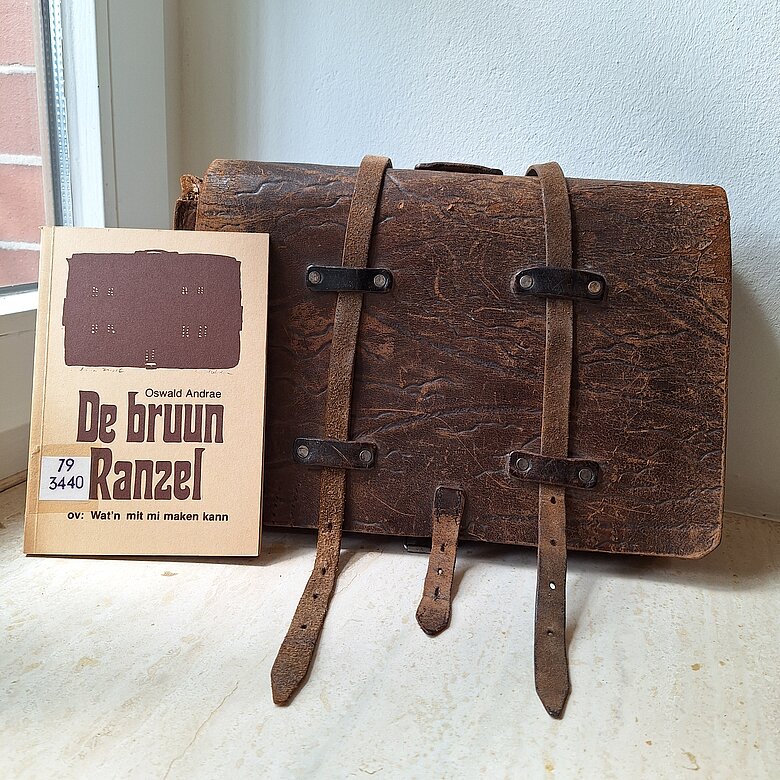 brauner Schulranzen mit Buch "De bruun Ranzel" im Vordergrund