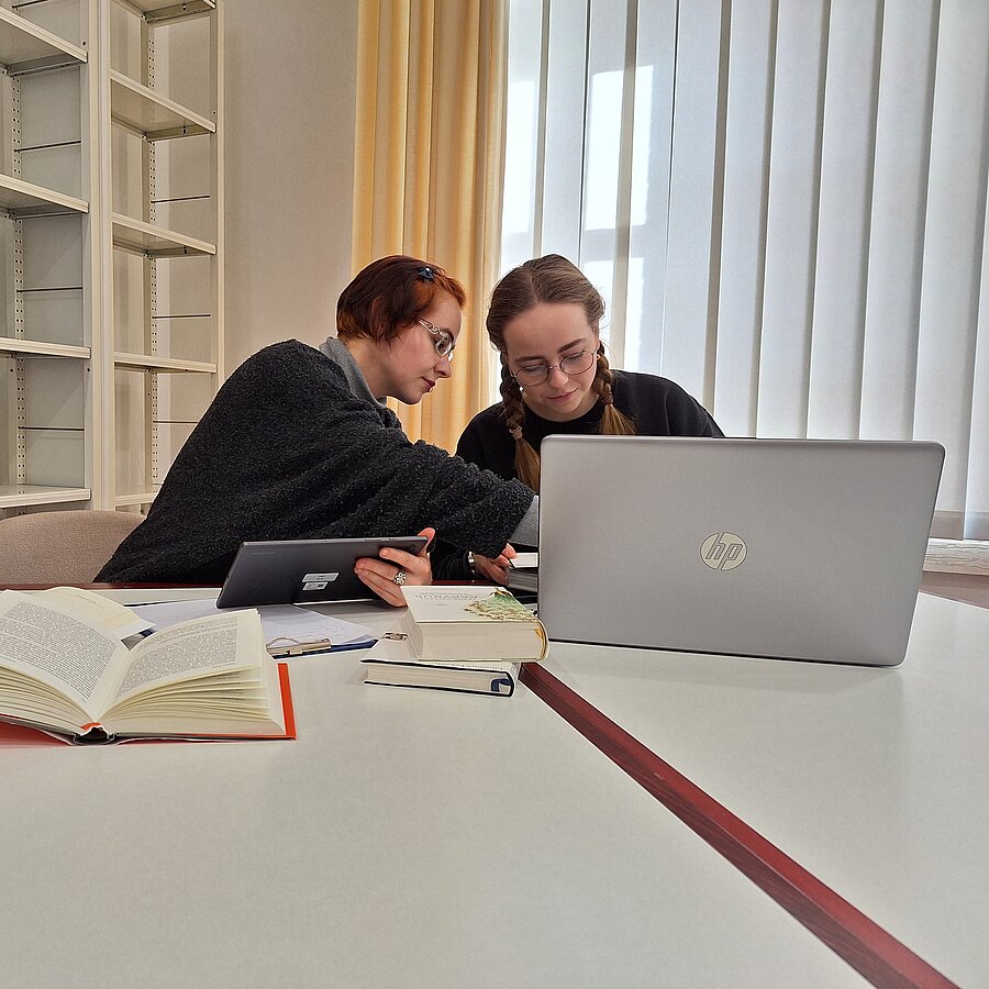 Zwei Schülerinnen sitzen vor einem Laptop gebeugt im Gruppenraum.