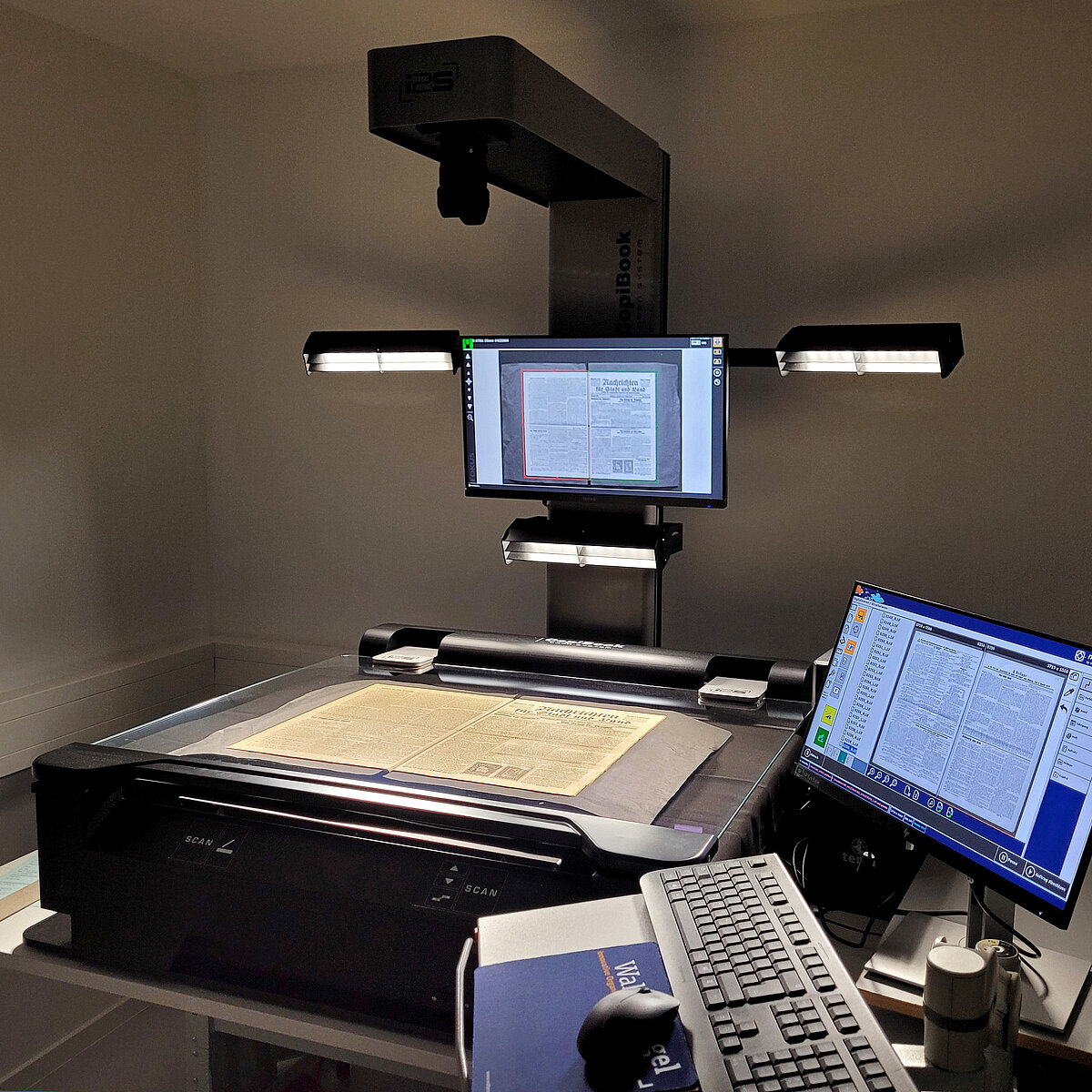 Totale des Zeitungsbandes auf dem Buchscanner. Computerbildschirm, Maus und Tastatur im Vordergrund.